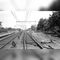 Zicht op de spoorlijn Utrecht-'s-Hertogenbosch in noordelijke richting gezien terhoogte van Station Houten bij het Stationserf met rechts in de verte De Graanmaalderij (Welkoop). Met aan beide zijde een geoderenspoor in de periode 1930-1955. Maker en bron onbekend.