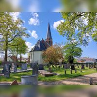De N>H. begraafplaats te Nederlangbroek gezien vanuit het het noorden met op de achtergrond de N.H. kerk aan de Brink 8 gezien in april 2022. Foto: Sander van Scherpenzeel.