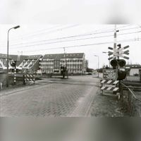 Zicht op de spoorwegovergang in de Staatslijn H vanaf de Vlierweg op de Standerdmolen met op de achtergrond het tijdelijke gemeentehuis van Houten (1981-1986). Spoorwegovergang is in 2000 gesloten en vervangen voor een fiets- en voetgangerstunnel in de periode 1981-1985. Bron: Regionaal Archief Zuid-Utrecht (RAZU), 353.