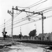 De spoorwegovergang met bovenleidingsportalen in augustus 1964 in de Vlierweg en Odijkseweg (Standerdmolen) gezien richting het zuidwesten, staande aan de oostkant van de spoorlijn. Bron: Het Utrechts Archief, catalogusnummer 166499.